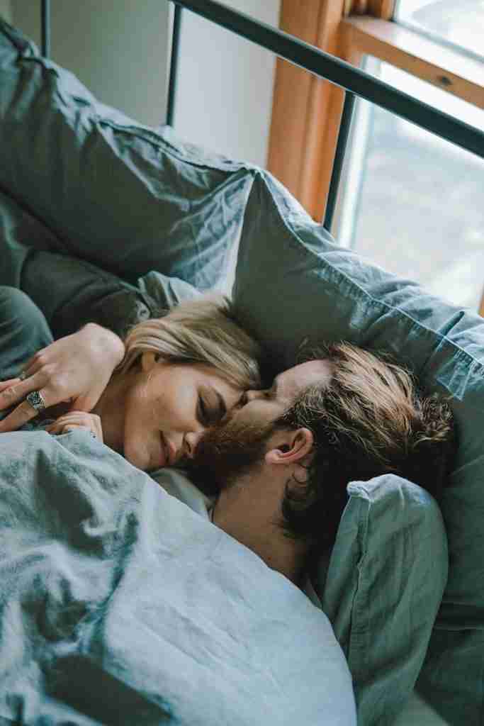 man kissing woman's forehead while lying on bed